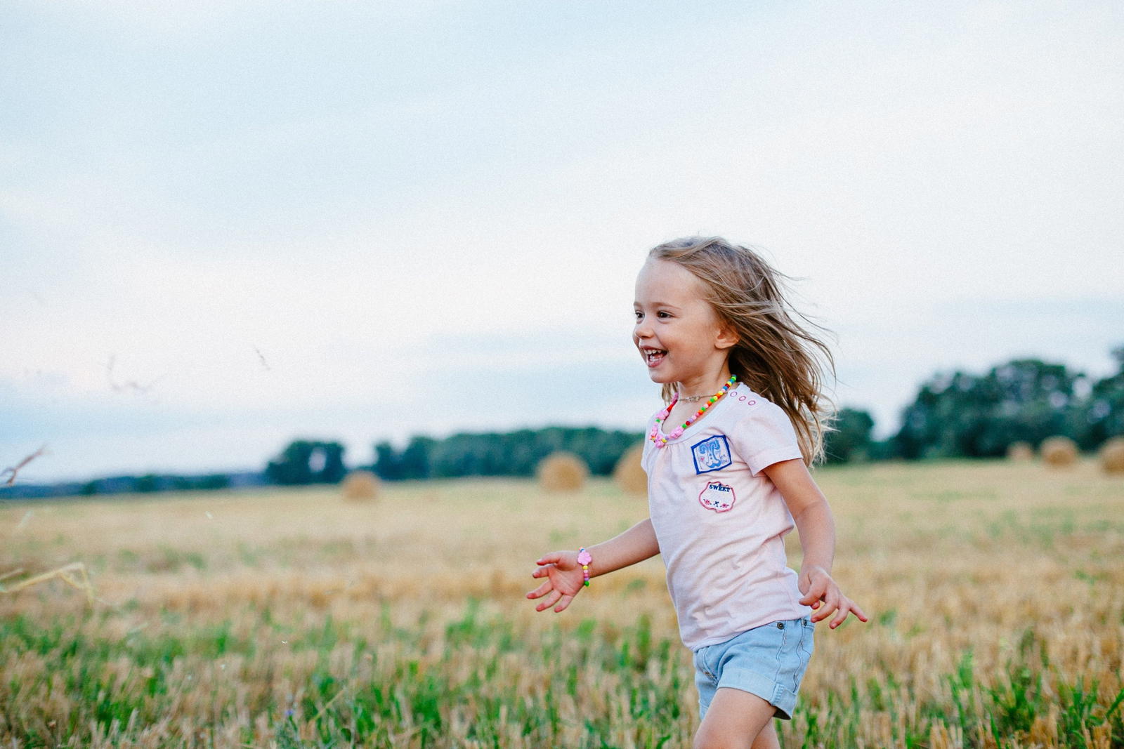 Smiling girl running through green field in summer