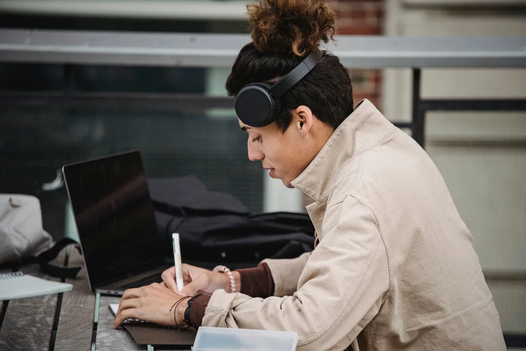 Young man with headphones taking notes while studying on laptop