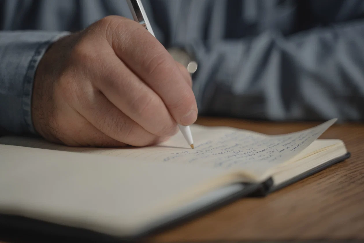 Close-up of hand writing in notebook — choosing the right words for test writing